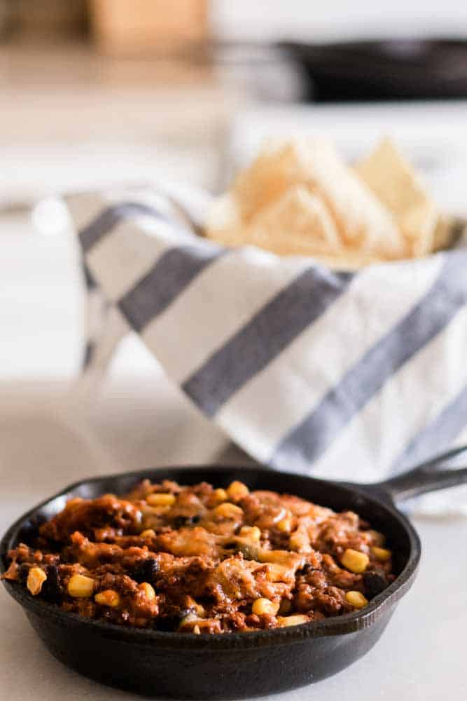 beef enchilada dip in a cast iron skillet with a basket of chips.