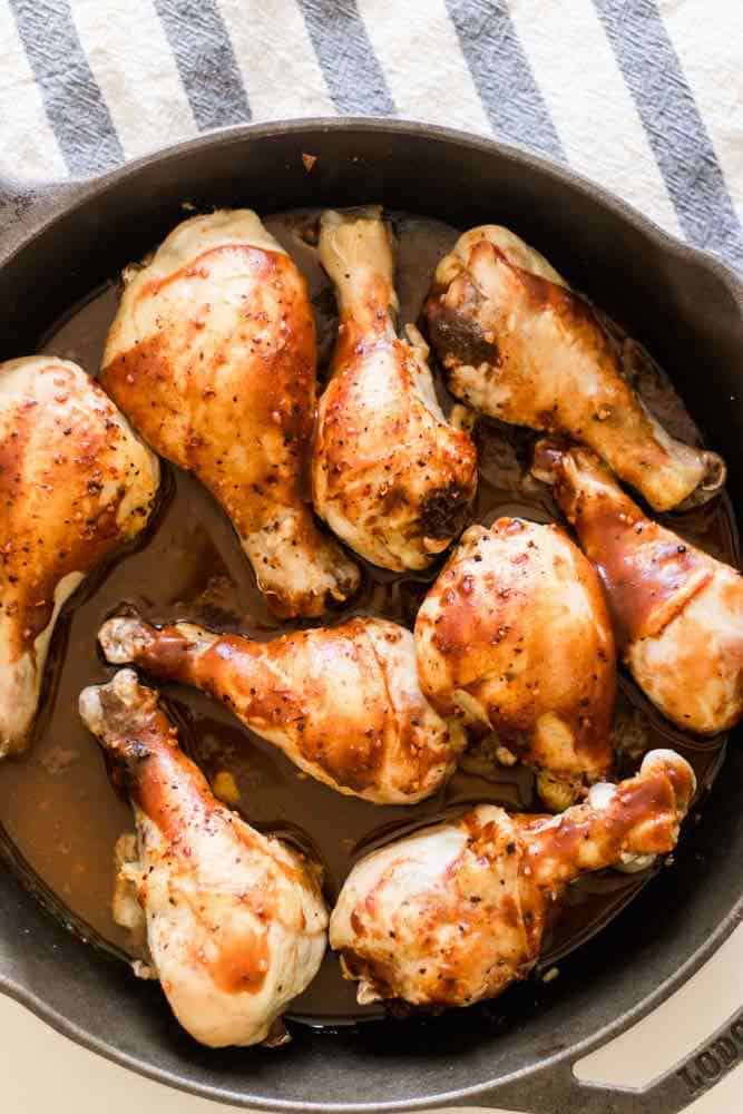 cast iron chicken drumsticks searing in a large skillet with barbecue sauce.