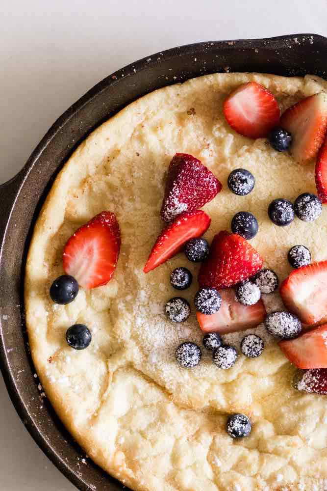 Dutch baby pancake in a cast iron skillet with strawberries and blueberries.