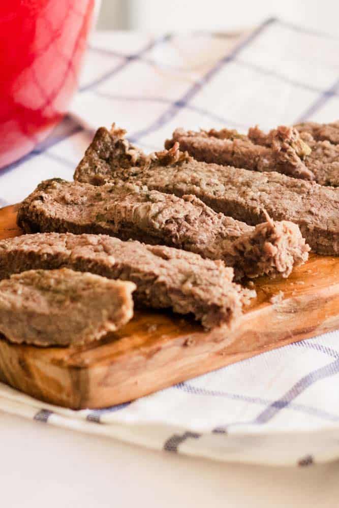 Thinly sliced round steaks on white marble with red dutch oven.