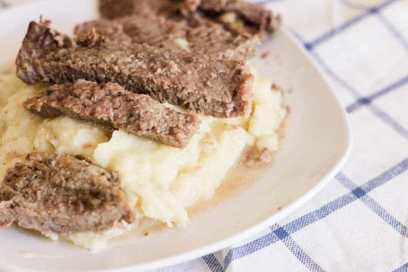 Sliced round steaks sitting on top of mashed potatoes.