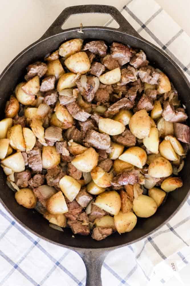 Steak and potatoes mixed up in a large cast iron skillet.