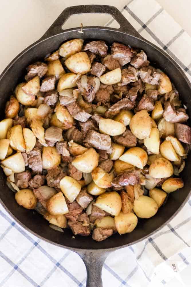 Steak and potatoes mixed up in a large cast iron skillet.