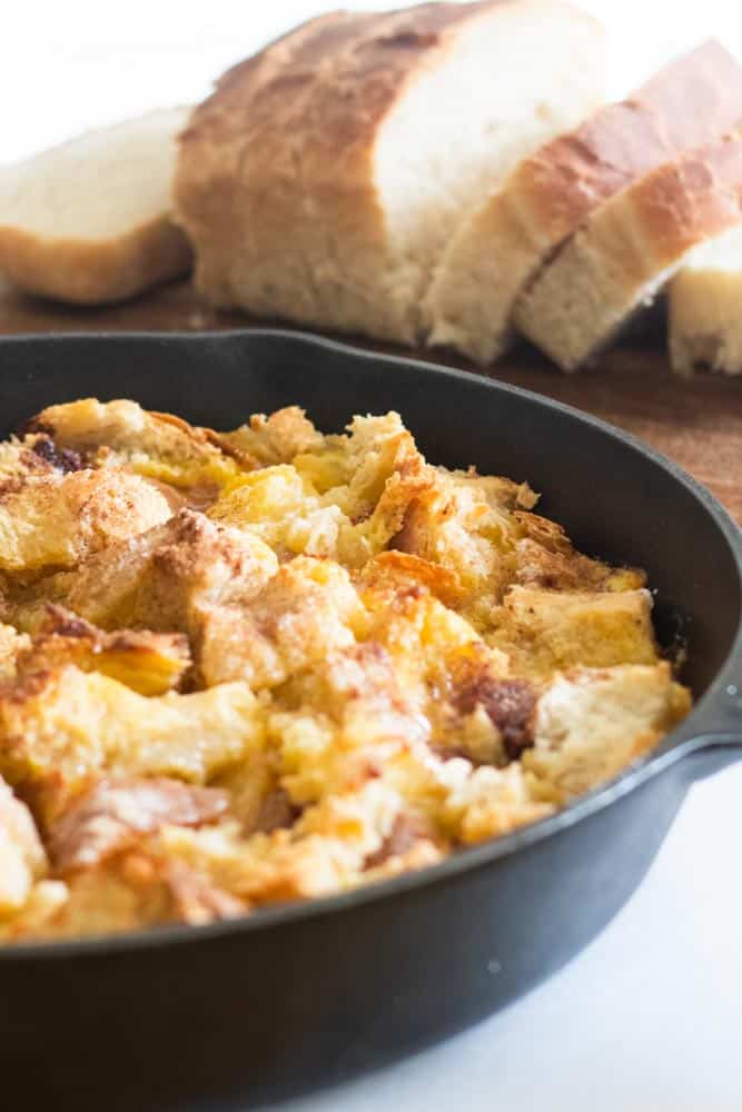 Large chunks of french bread flooded with french toast filling in a cast iron skillet.