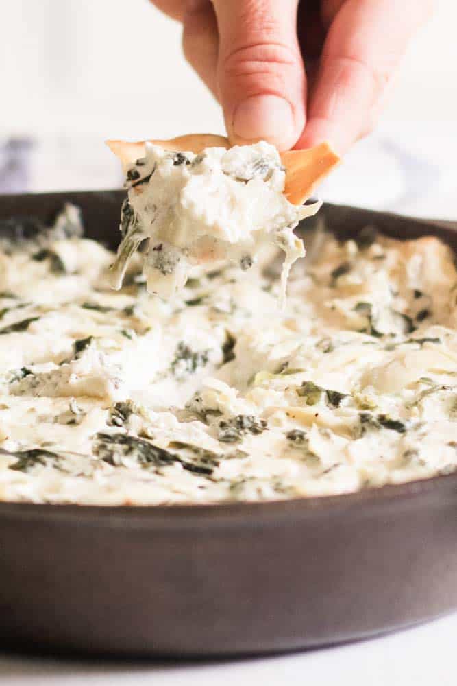 Scooping out some steaming hot artichoke dip from a cast iron skillet.