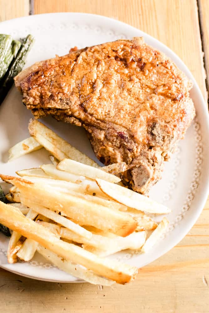 Southern fried pork chop with homemade fries and asparagus on dinner plate.