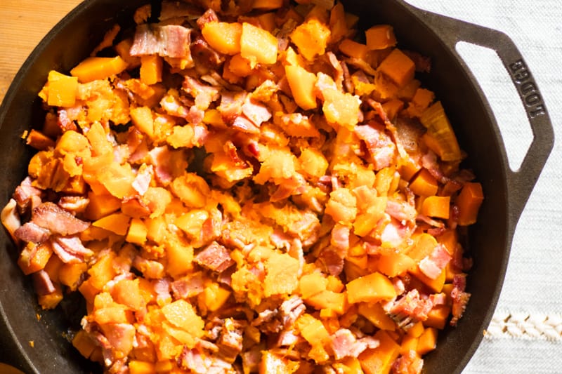 Bacon and diced butternut squash in a cast iron skillet.