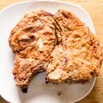 2 southern fried bone in pork chops on white serving plate.
