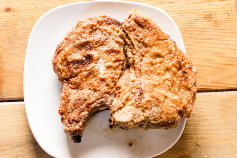 2 southern fried bone in pork chops on white serving plate.