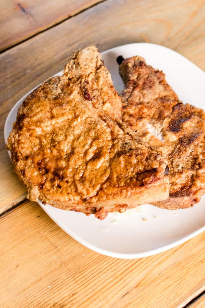 Juicy tender breaded and fried pork chops, bone-in on white dinner plate.