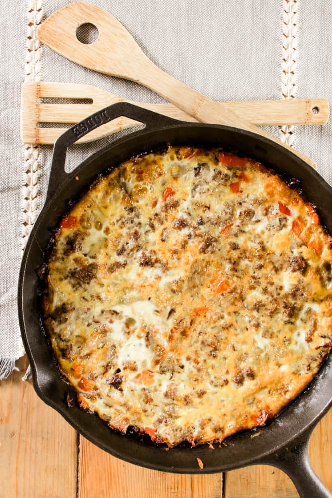 Sausage, egg and cheese breakfast casserole in a cast iron skillet on a wooden table with wooden serving utensils.