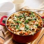 dutch oven goulash topped with cheese and fresh parsley on a wooden farm table.