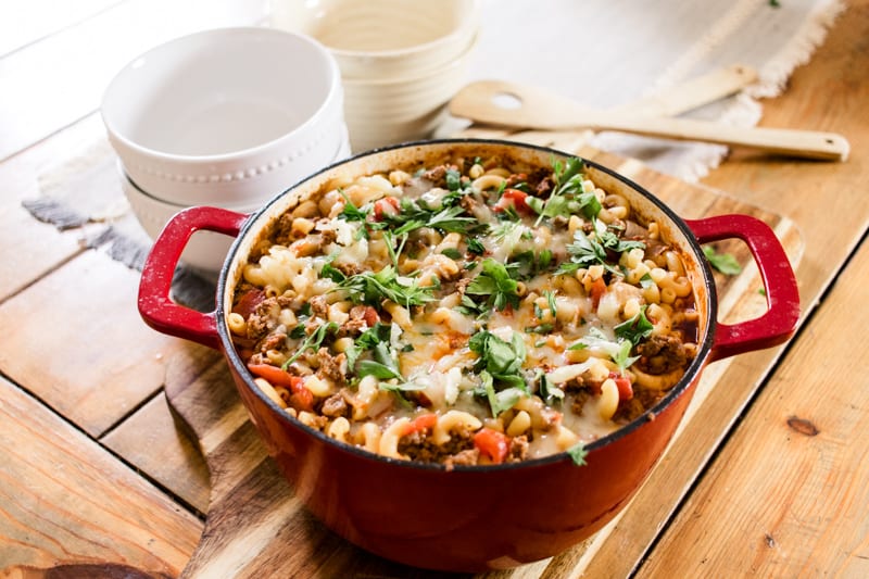 dutch oven goulash topped with cheese and fresh parsley on a wooden farm table.