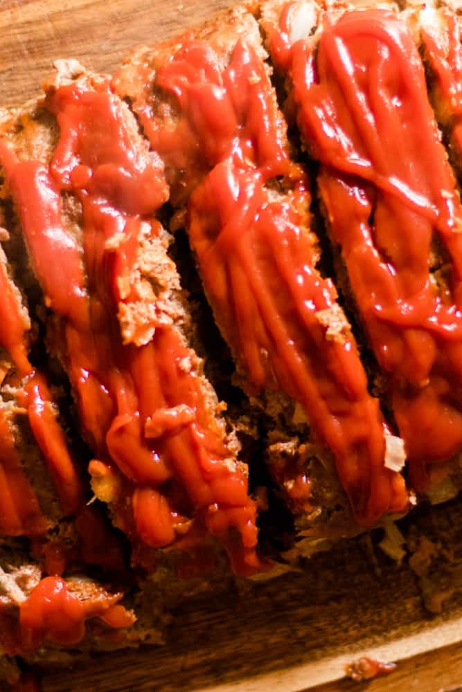 Homestyle meatloaf on wooded cutting board with drizzles of ketchup.