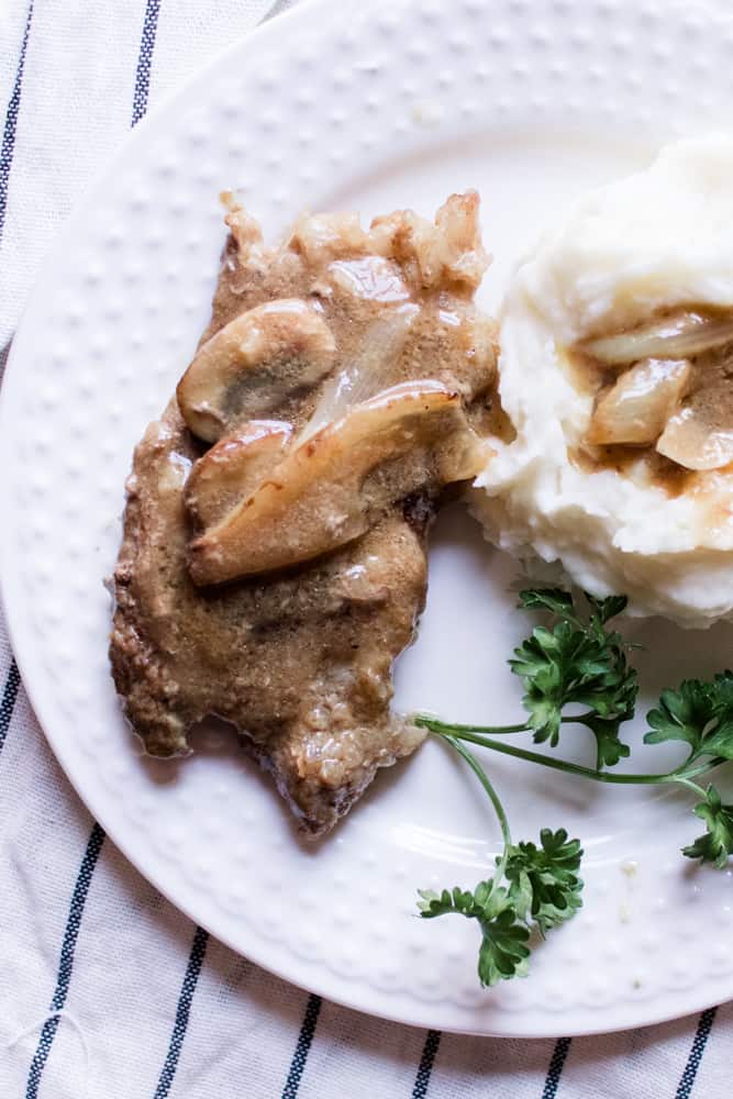 Dinner plate of round steak, gravy, mushrooms, onions and mash potatoes.