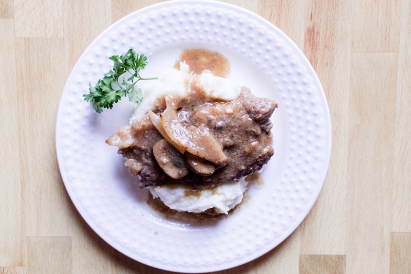 Stove top round steak on white plate with parsley and gravy on mashed potatoes.