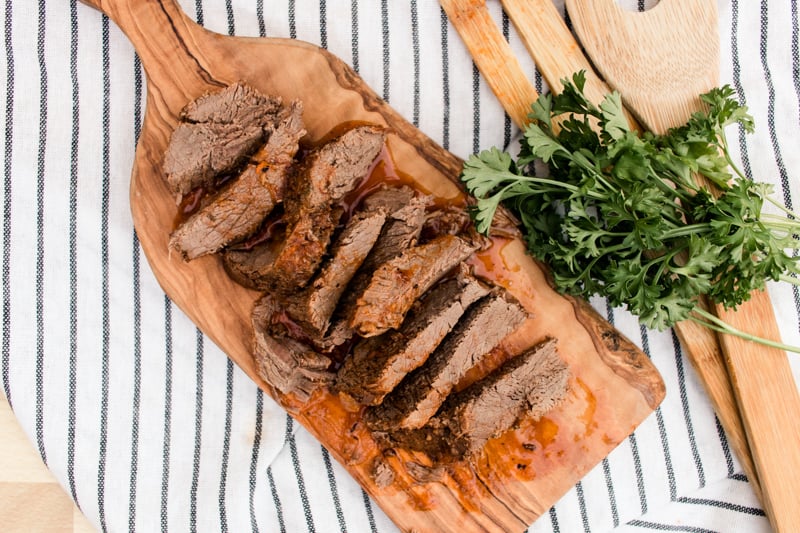 Sliced oven baked venison roast on wooden cutting board with fresh parsley