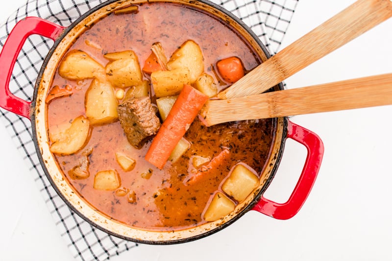 Venison stew in dutch oven with two wooden serving spoons.