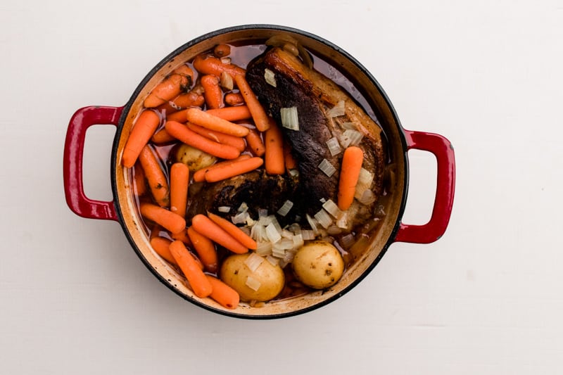 Homemade beef brisket in a red dutch oven with carrots and potatoes.