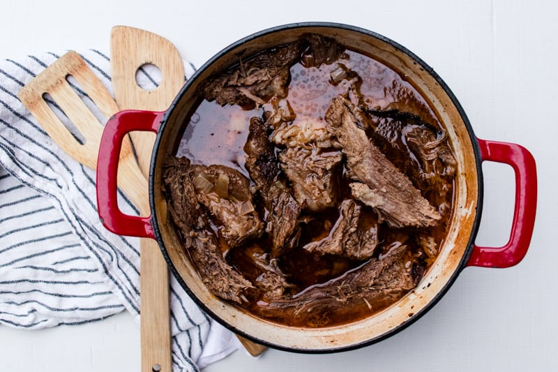 Sliced brisket  meat in beef broth on white marble.