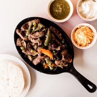 Venison fajitas on a cast iron fajita skillet with fresh salsa, sour cream and shredded cheese.