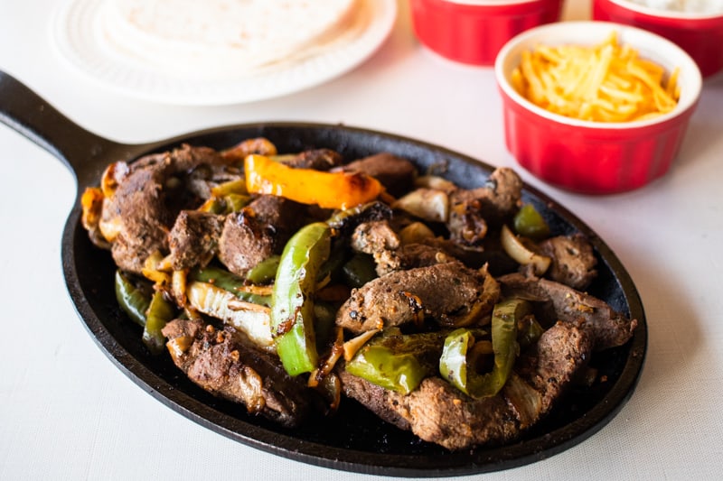 Texas fajitas in a fajita skillet along with a ramekin of cheese.