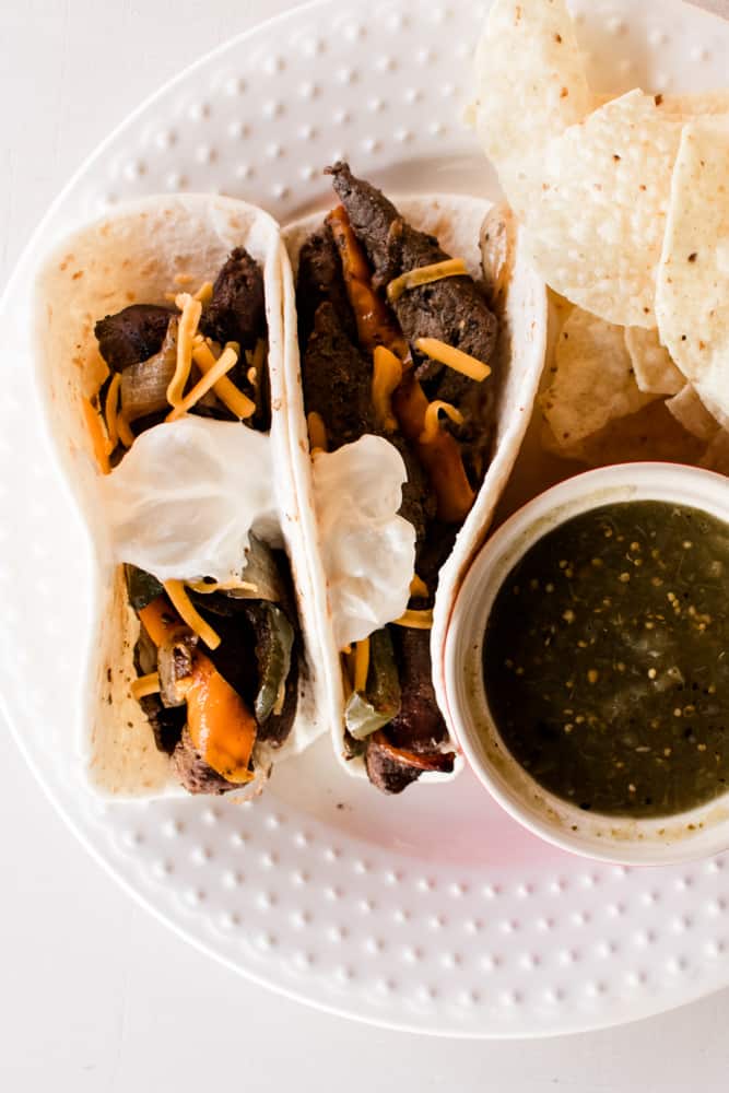 Cast iron fajitas on a white plate with chips and salsa.