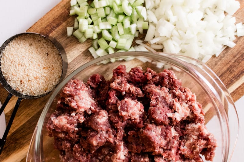 Chopped celery, onions, bread crumbs, seasonings and ground deer and pork sausage on a wooden cutting board.