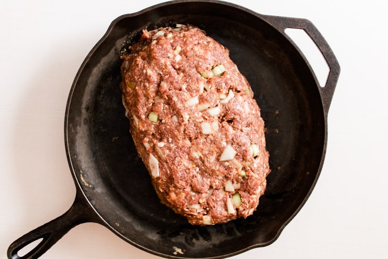 A loaf of homemade venison meatlof in a large cast iron skillet.