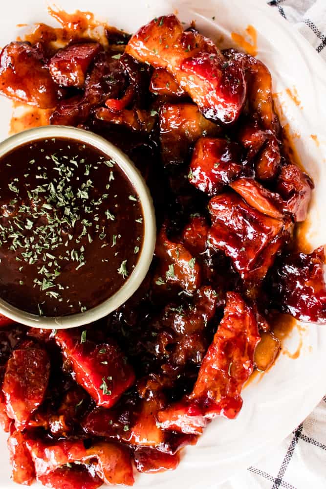 Burnt ends pork belly on serving platter sprinkled with parsley.