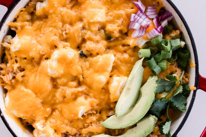 Mexican chicken casserole layered into a red dutch oven on a white marble countertop with fresh veggies on top.
