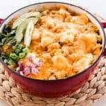 Dutch oven chicken casserole topped with melted cheese and fresh green onions, red onions and fresh avocado slices.