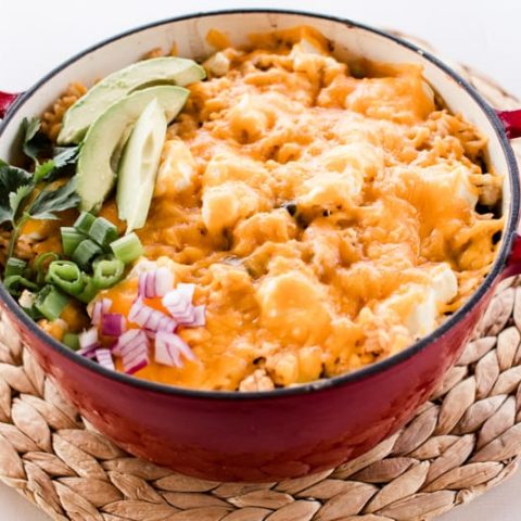 Dutch oven chicken casserole topped with melted cheese and fresh green onions, red onions and fresh avocado slices.