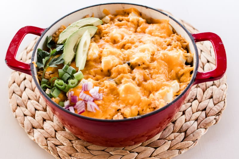 Dutch oven chicken casserole topped with melted cheese and fresh green onions, red onions and fresh avocado slices.