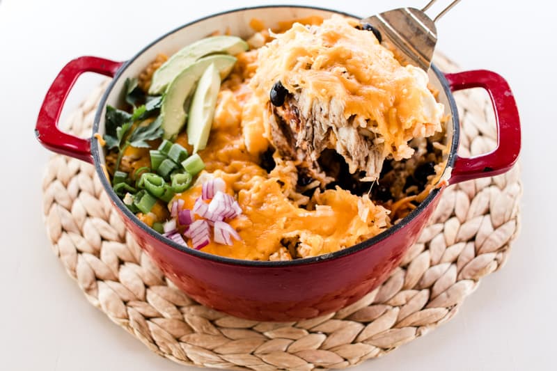 Scooping southwest chicken casserole out of a red dutch oven.