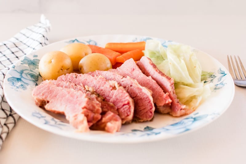 Dutch oven corned beef on flowered plate with cabbage, new potatoes and carrots.