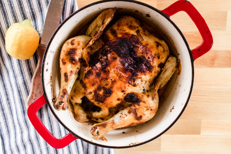 Dutch oven whole chicken with an extra crispy crust, cutting knife and fresh lemon.