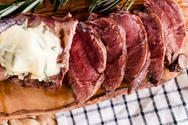 Elk tenderloin cook to about medium on a wooden cutting board with a homemade garlic butter.