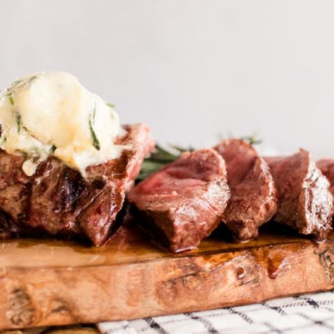 Elk tenderloin marinated in butter on a decorative wooden board.