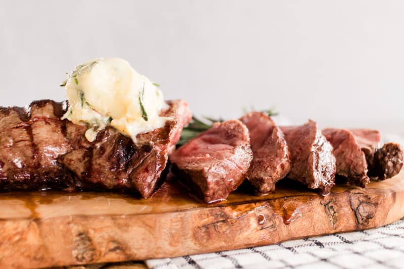 Elk tenderloin marinated in butter on a decorative wooden board.