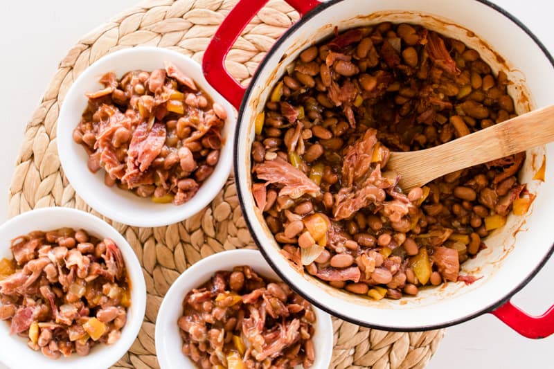 Dutch oven full of baked beans and ham being scooped out into individual bowls.