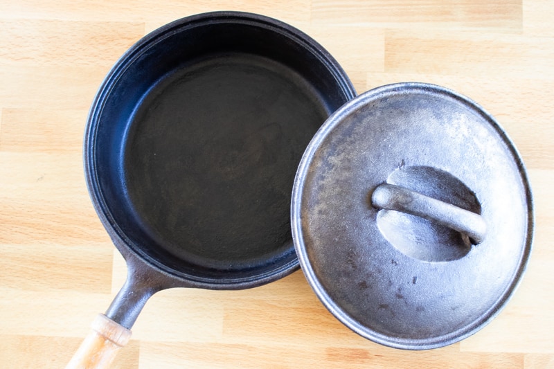 A clean cast iron skillet with lid and wooden handle on butcher block countertop.