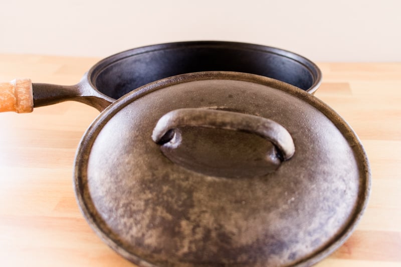 Freshly cleaned cast iron skillet and skillet lid with a wooden handle on butcher block countertop.