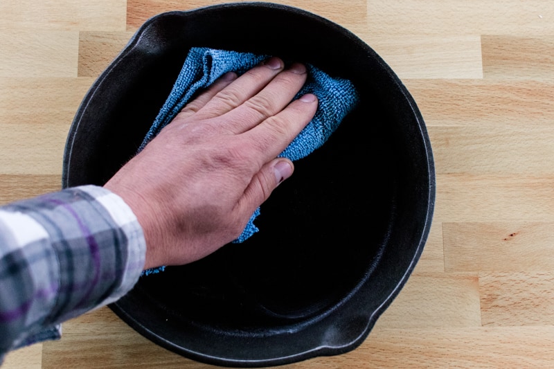 Wiping oil on a cast iron skillet to prevent it from rusting.