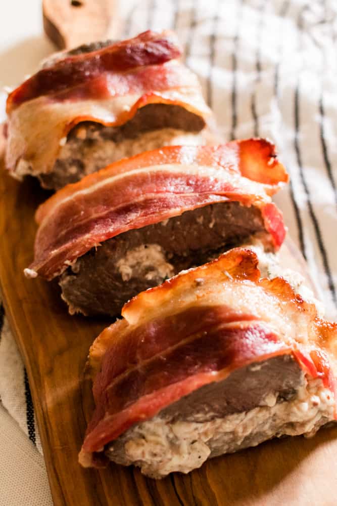 Bacon wrapped venison tenderloin with homemade filling on a marble countertop.