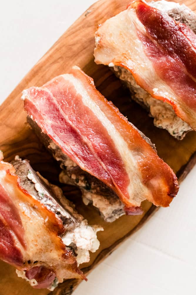 Backstrap cut into pieces, stuffed with cream cheese filling and wrapped in crispy bacon on a small wooden cutting board.