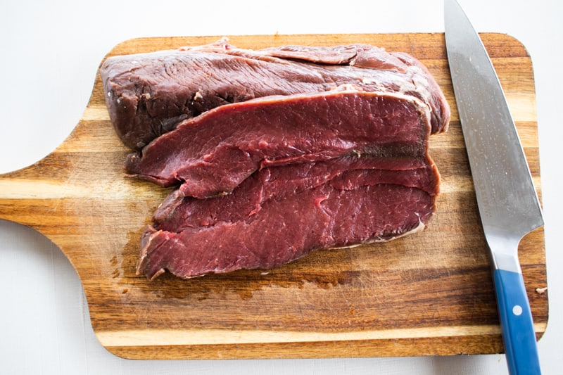 A deer backstrap split open on a cutting board.