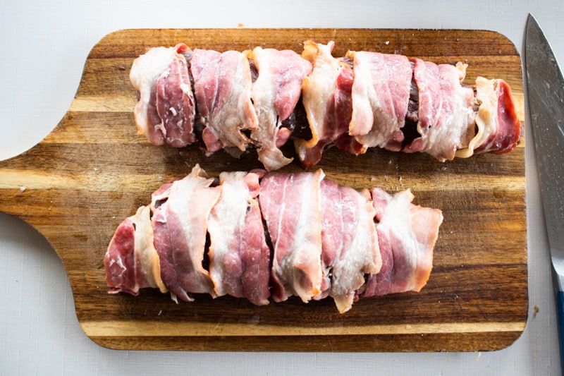 Bacon wrapped tenderloin on a wooden cutting board.