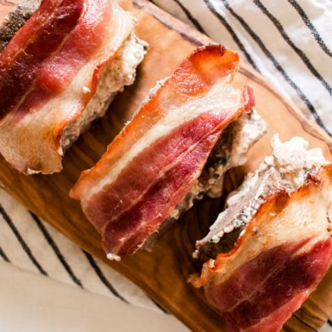 Bacon wrapped deer tenderloin on a cooking towel and a marble kitchen counter.