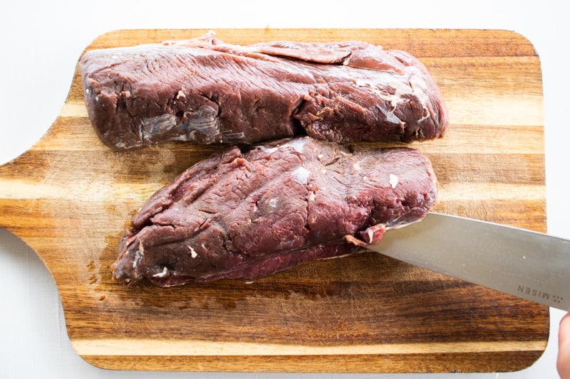 Slicing a venison backstrap lengthwise with a sharp knife.